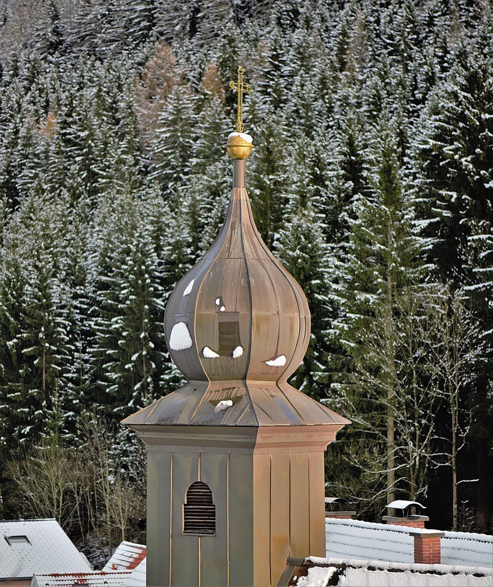 Ein Kirchturm im Winter mit einem Blechdach